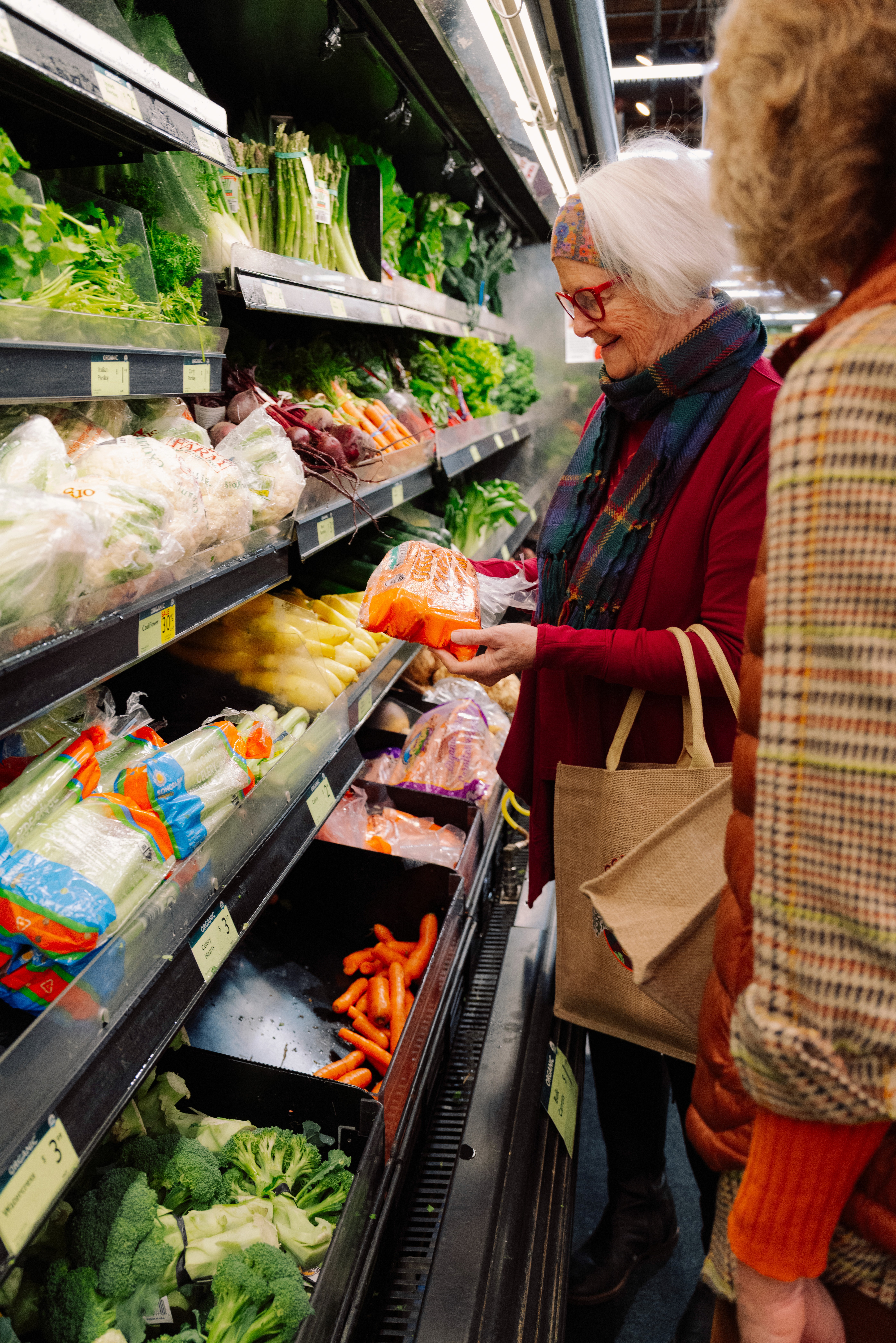 A store employee in an apron holds up two items in front of a colorful produce display.