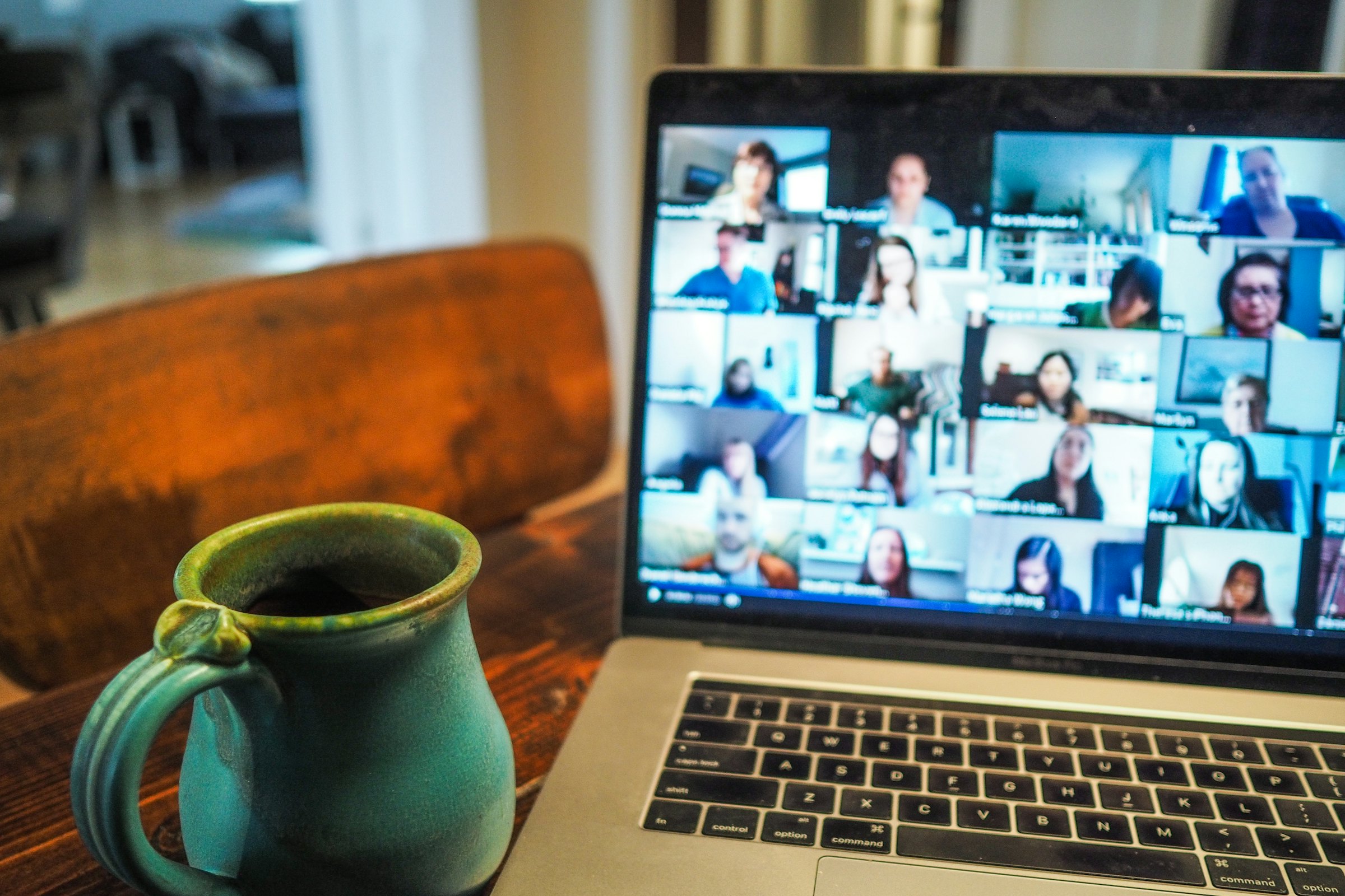 A laptop showing a grid video call beside a coffee mug