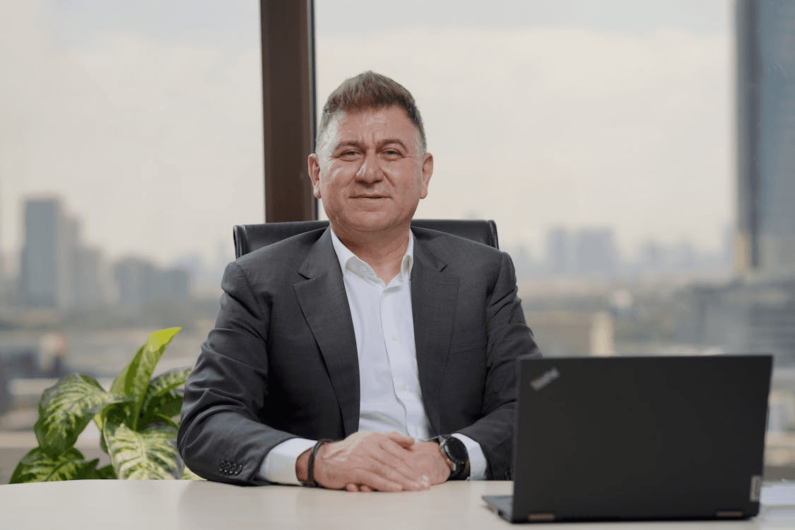 Corporate individual seated with a laptop, against a blurred glassy background