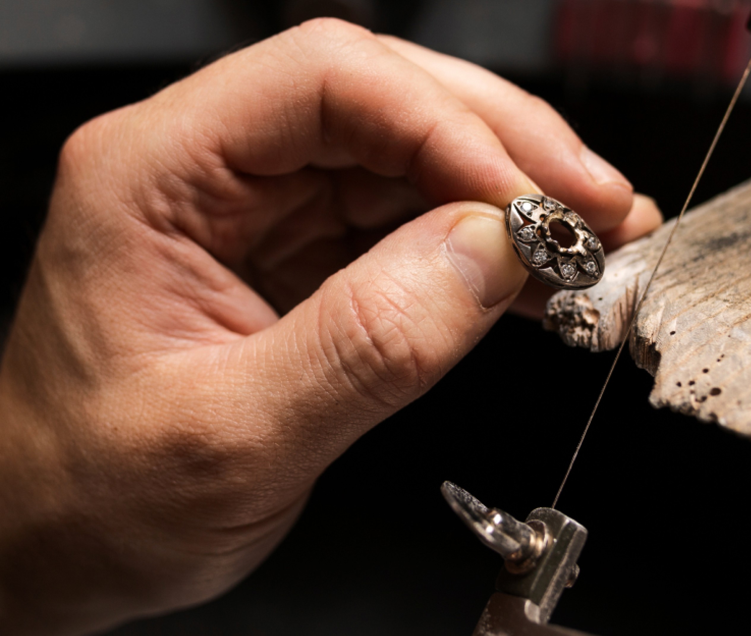 Close-up of a hand holding a detailed, ornate ring with intricate designs and small gemstones, being worked on with precision tools.