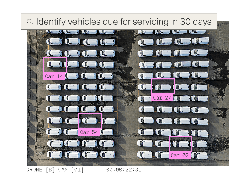Aerial drone view of a large parking lot with several vehicles highlighted by pink bounding boxes for fleet servicing identification.