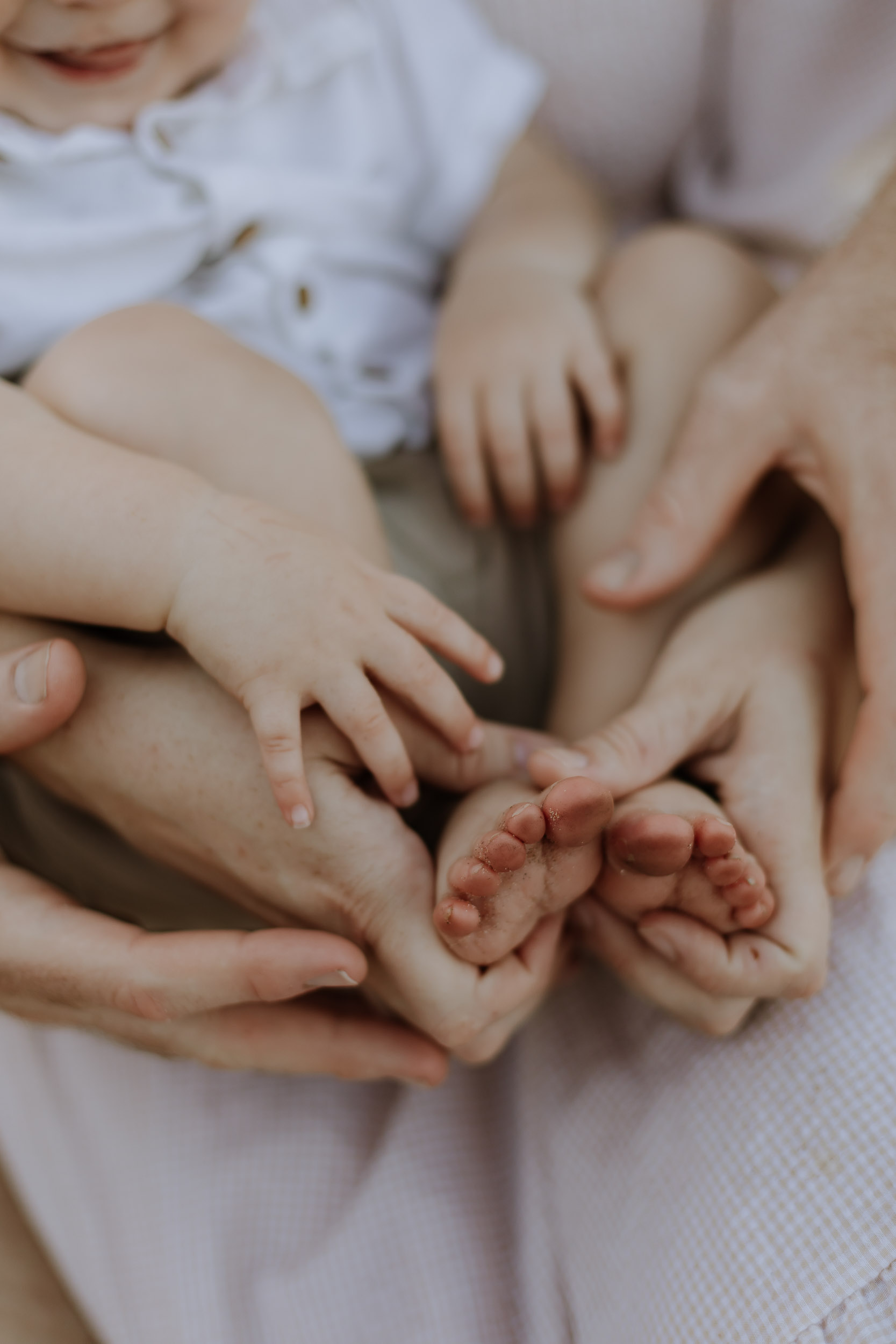 Close up image of mother holding son's feet while sitting in the grass in lifestyle photography session