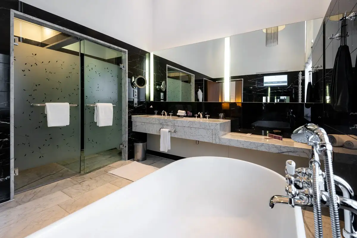 A modern bathroom with a walk-in glass shower, a double vanity with marble countertops, and a large white soaking tub.