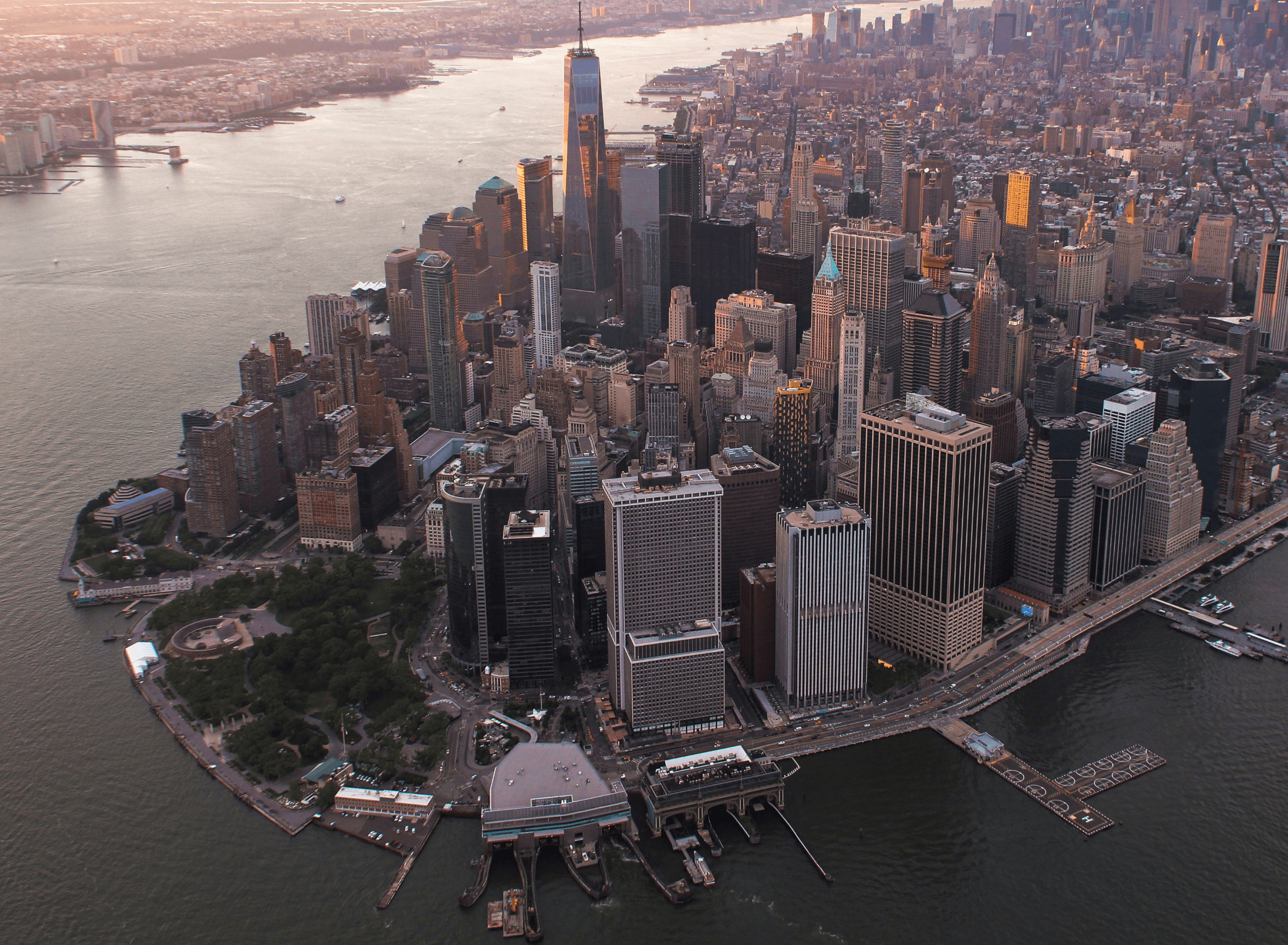 Aerial view of a city skyline at sunset, with skyscrapers along a waterfront and the river winding through.