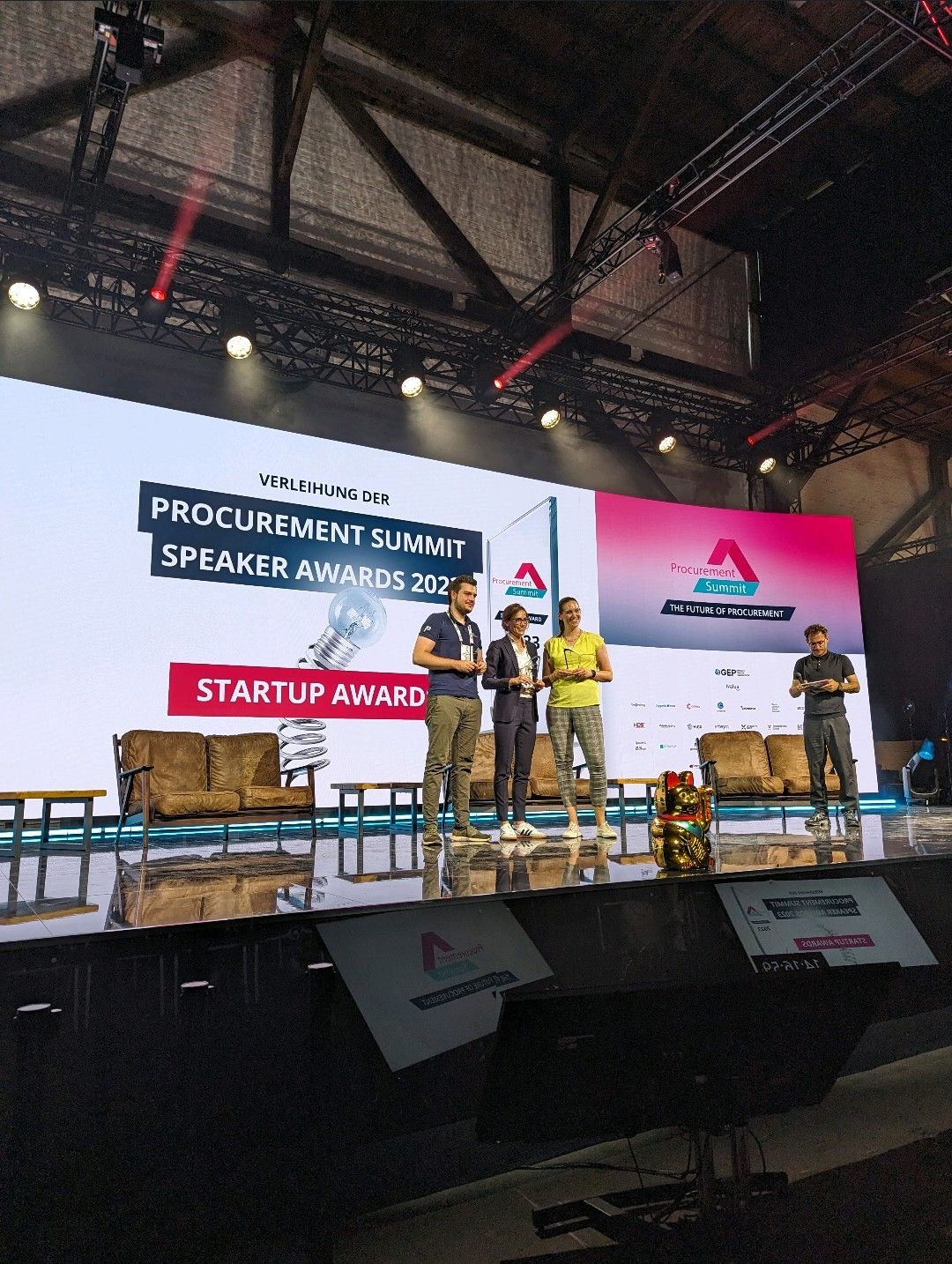 A group of three people stand on stage holding an award at the Procurement Summit, with a large digital screen displaying "Speaker Awards 2023" and "Startup Award" in the background.