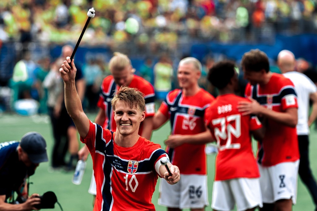Martin Odegaard holds drum mallets while celebrating with Erling Haaland and Norway teammates after beating Brazil