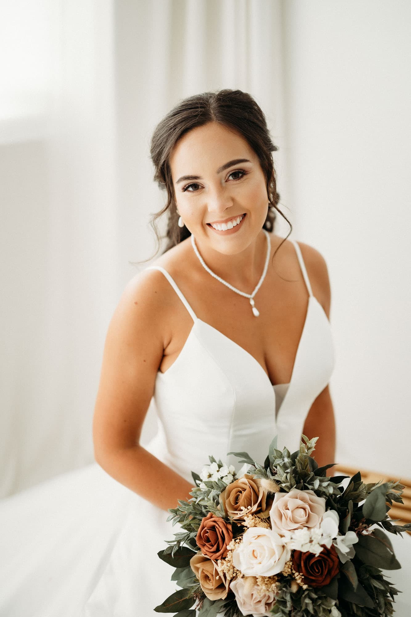 A close-up portrait of a bride smiling warmly at the camera while holding a bouquet, shot at Revelator Studio, a natural light studio in Shreveport.