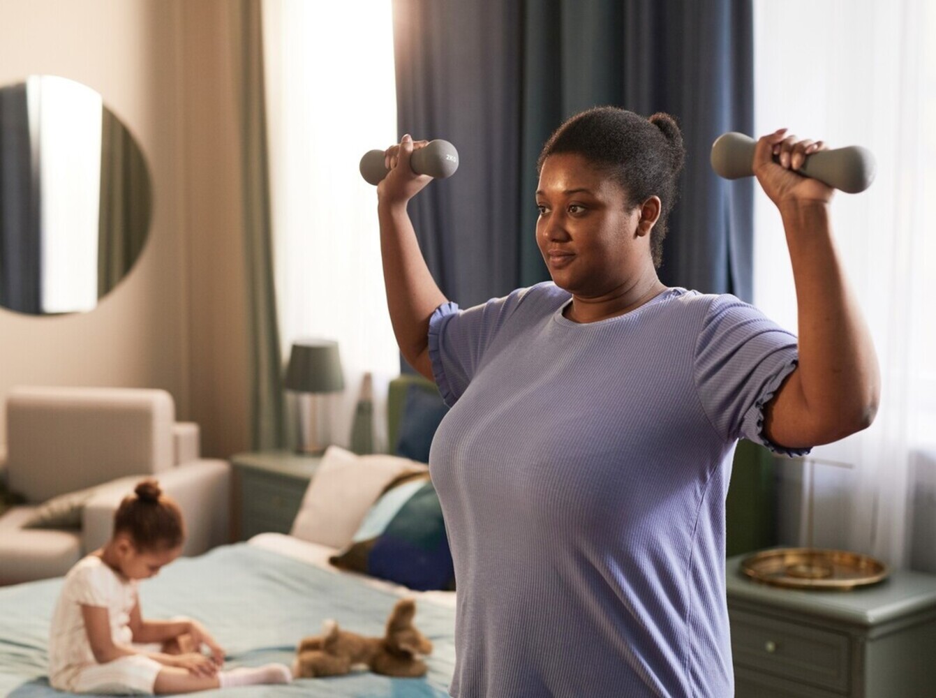 mother learning how to lose weight lifting weights by using light dumbbells to exercise in her home