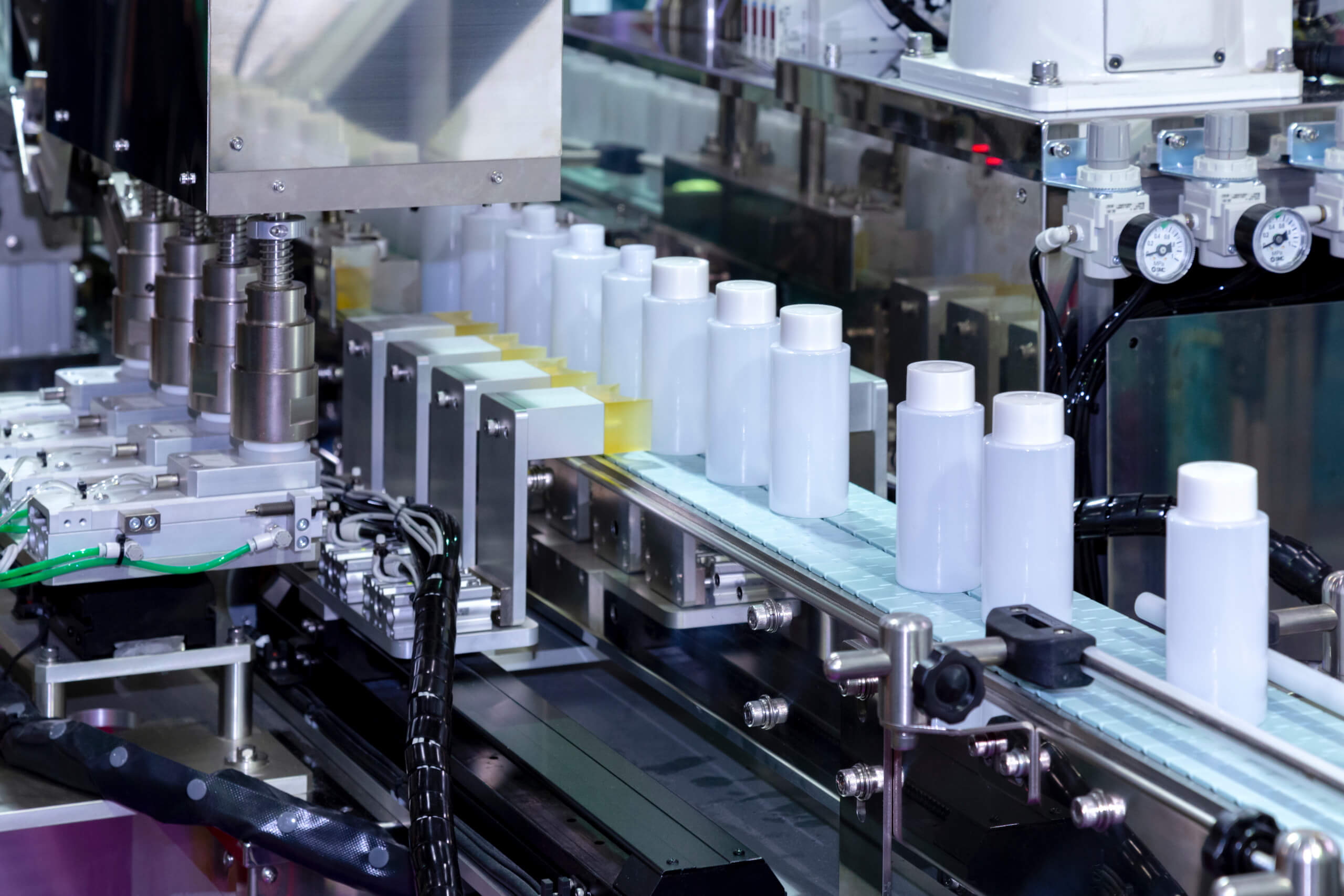 White cosmetic bottles moving along an automated production line conveyor.