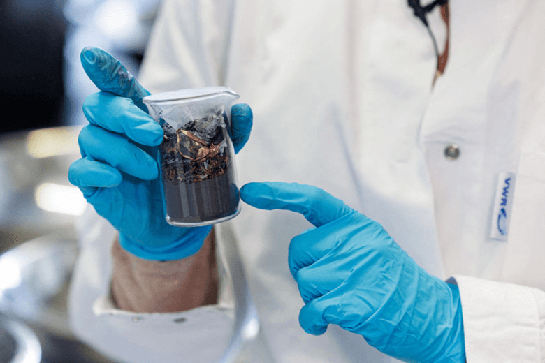 Title: Researcher holding crushed lithium-ion battery material containing dark electrode powder and copper and aluminium foil fragments. - Description: Researcher holding crushed lithium-ion battery material containing dark electrode powder and copper and aluminium foil fragments.