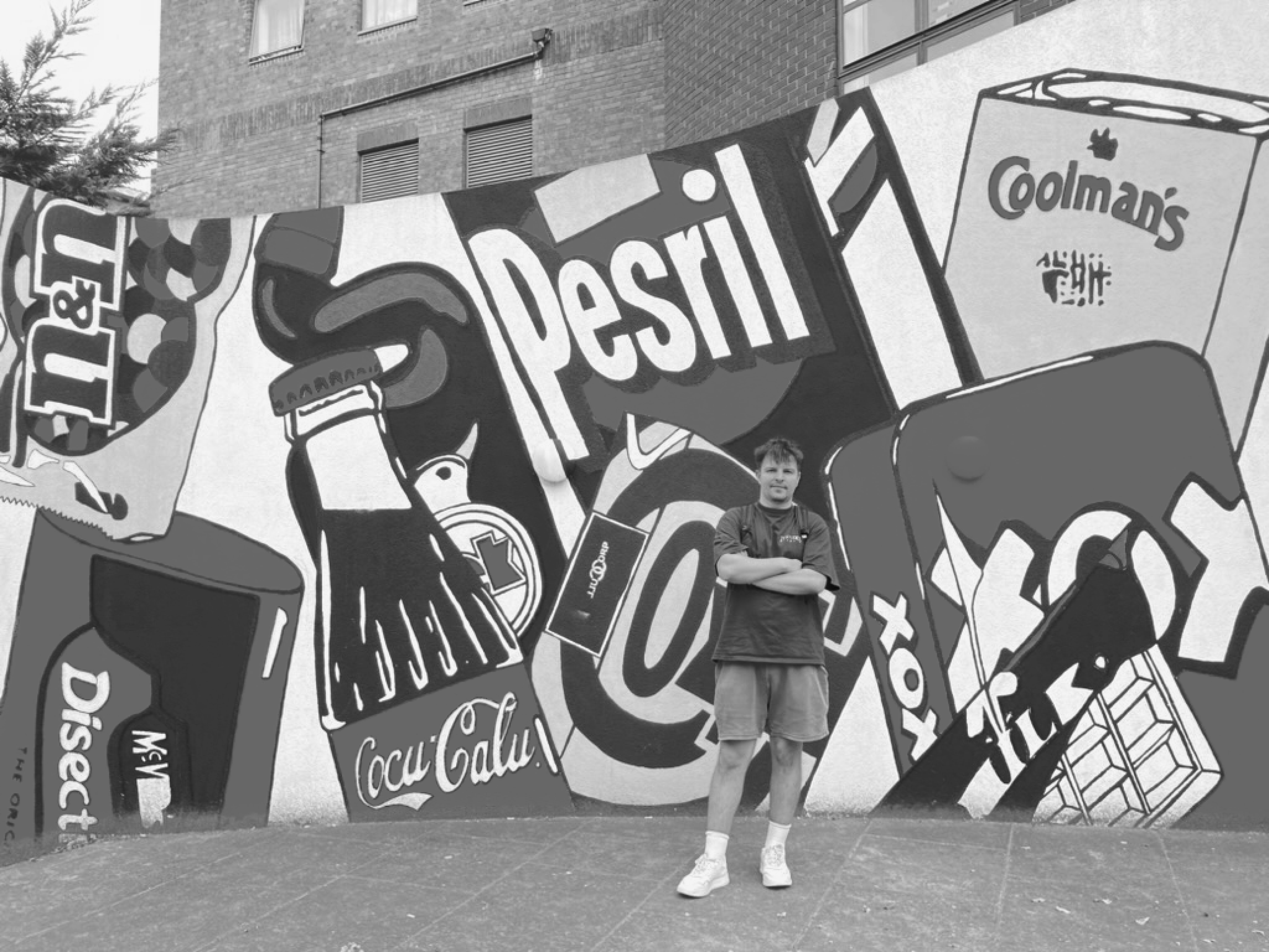 Kamil Zieliński standing next to the Musuem Brandu in London. In the background, there's a graphic featuring counterfeit names of iconic products such as "pesril" and "coca-calu."
