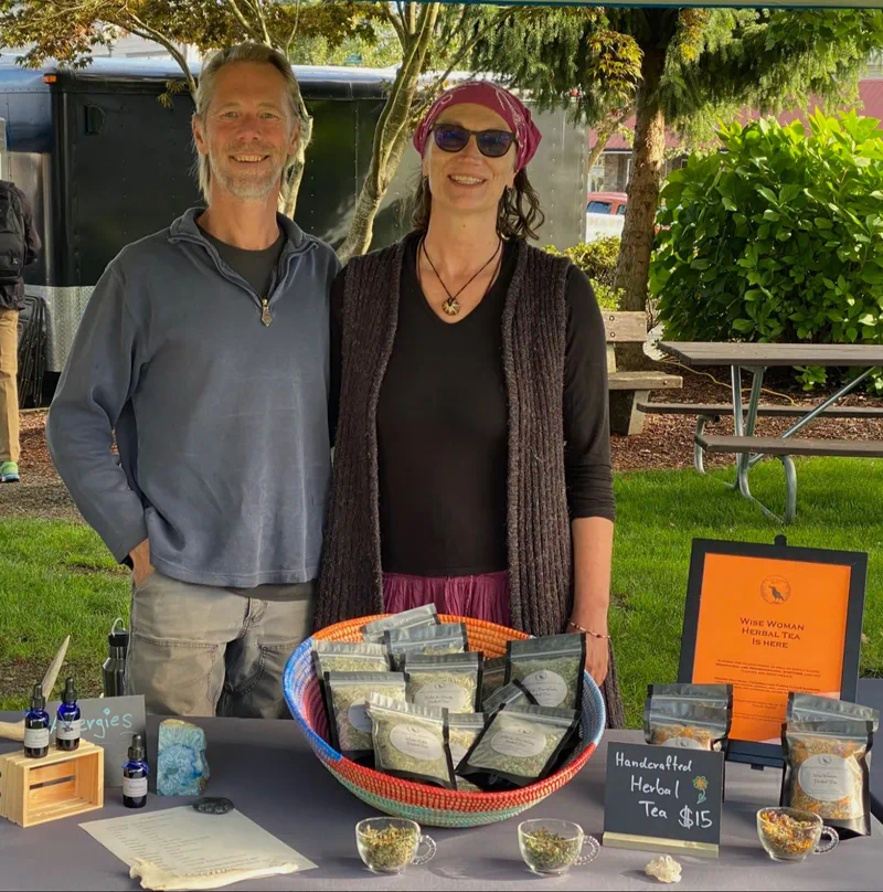 The owners of River Raven Herbs standing behind a table displaying their herbal products.