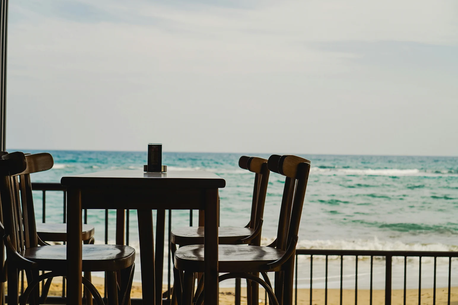 Outdoor dining table and chairs on a beachfront terrace overlooking the sea.