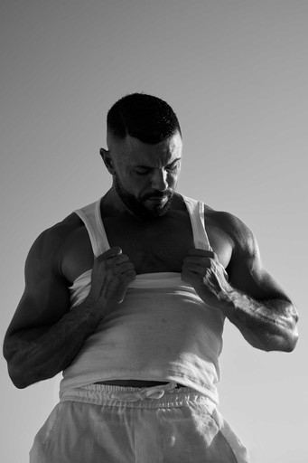 Hombre musculoso con camiseta blanca y pantalones cortos posando en el estudio, mostrando su físico, ideal para fotografía de moda, fitness o retrato, resaltando la calidad y la excelencia en un entorno de Palma, Mallorca, perfecto para fotografía comercial y diseños de vanguardia.