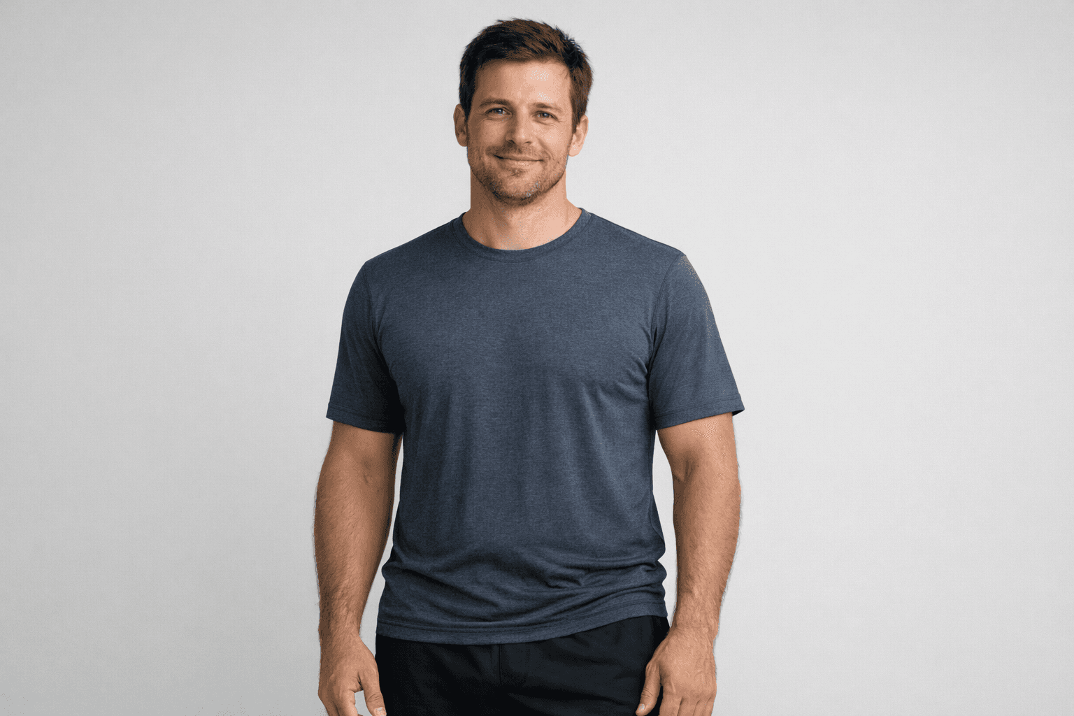 Fit man in a charcoal grey t-shirt smiling against a plain white studio background.