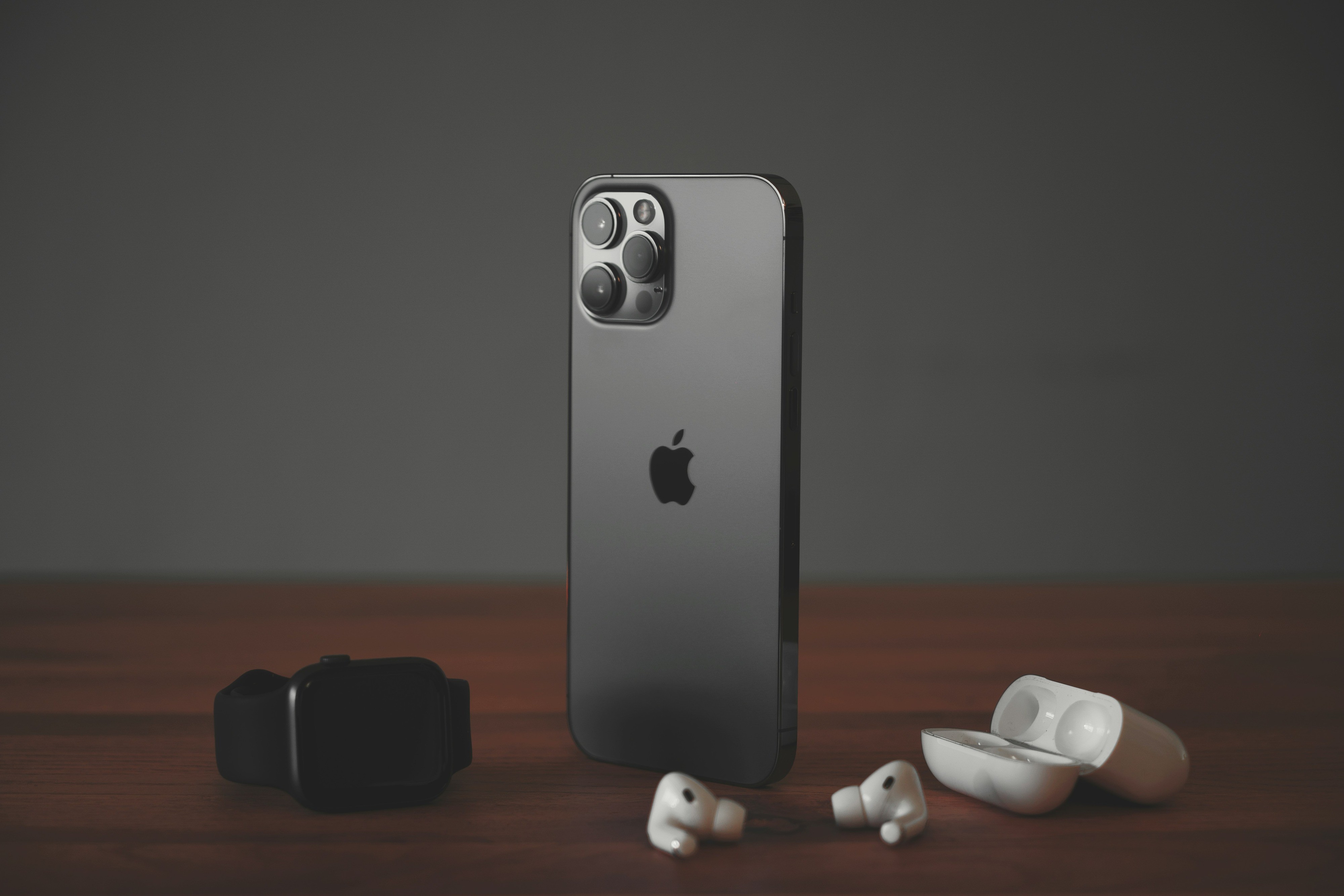  Sleek iPhone with a metallic finish stands upright, accompanied by AirPods and an Apple Watch, showcasing Apple's premium tech accessories.