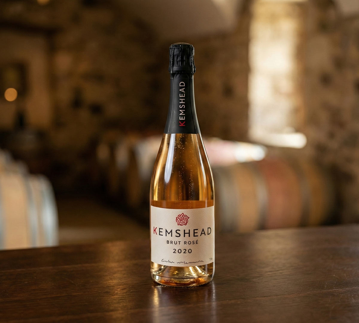 An image of a bottle of Kemshead Brut Rose sparkling wine in a rustic wine cellar.