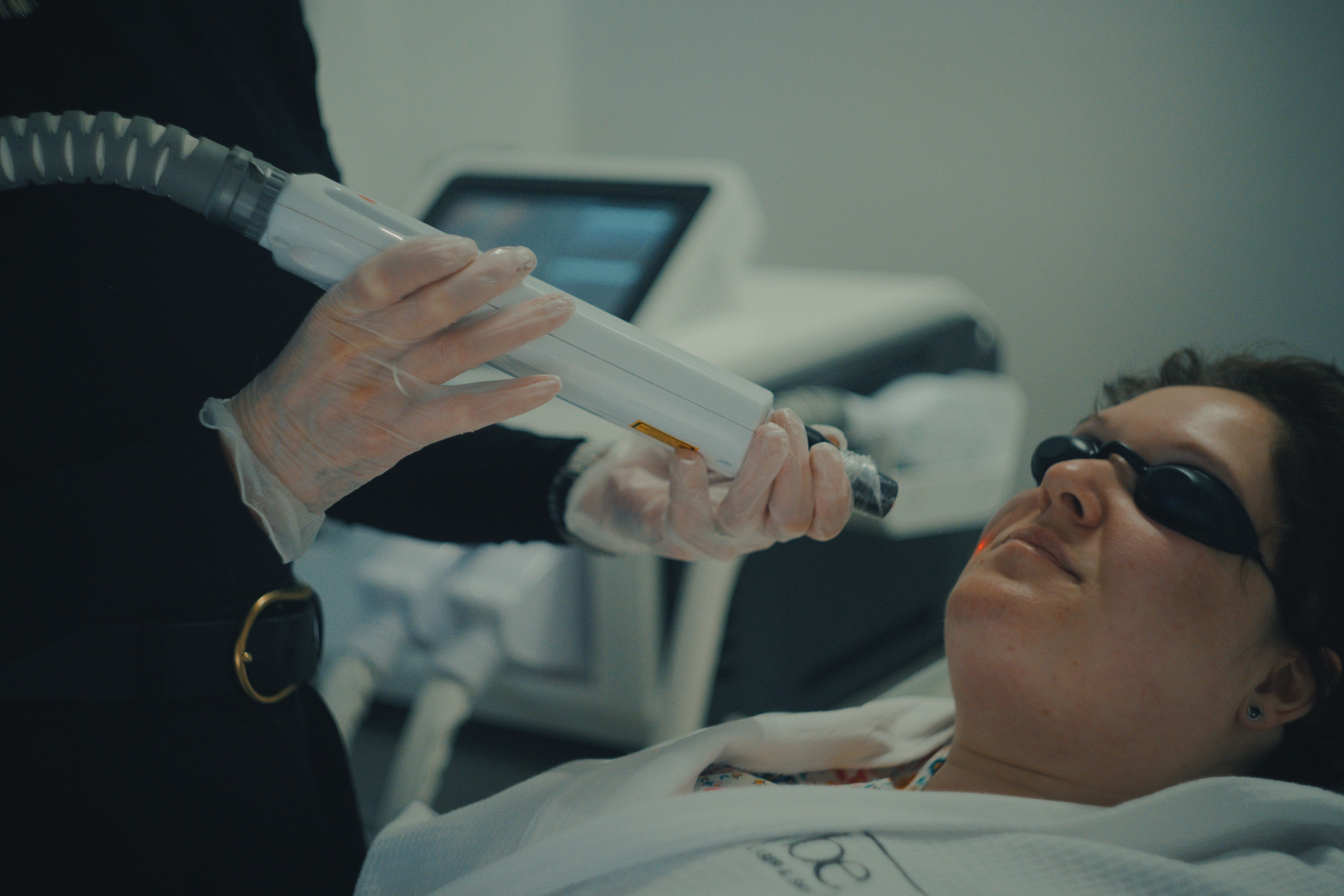 Hands in gloves holding a laser device near a person's face.