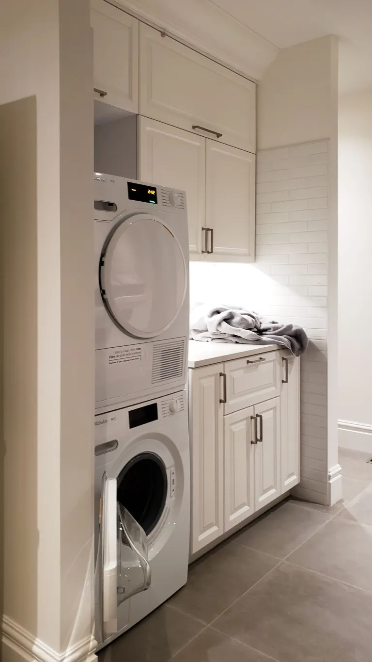 Image of Laundry room with stacked washer and dryer, white cabinets, and modern tile flooring, KHD Homes design.