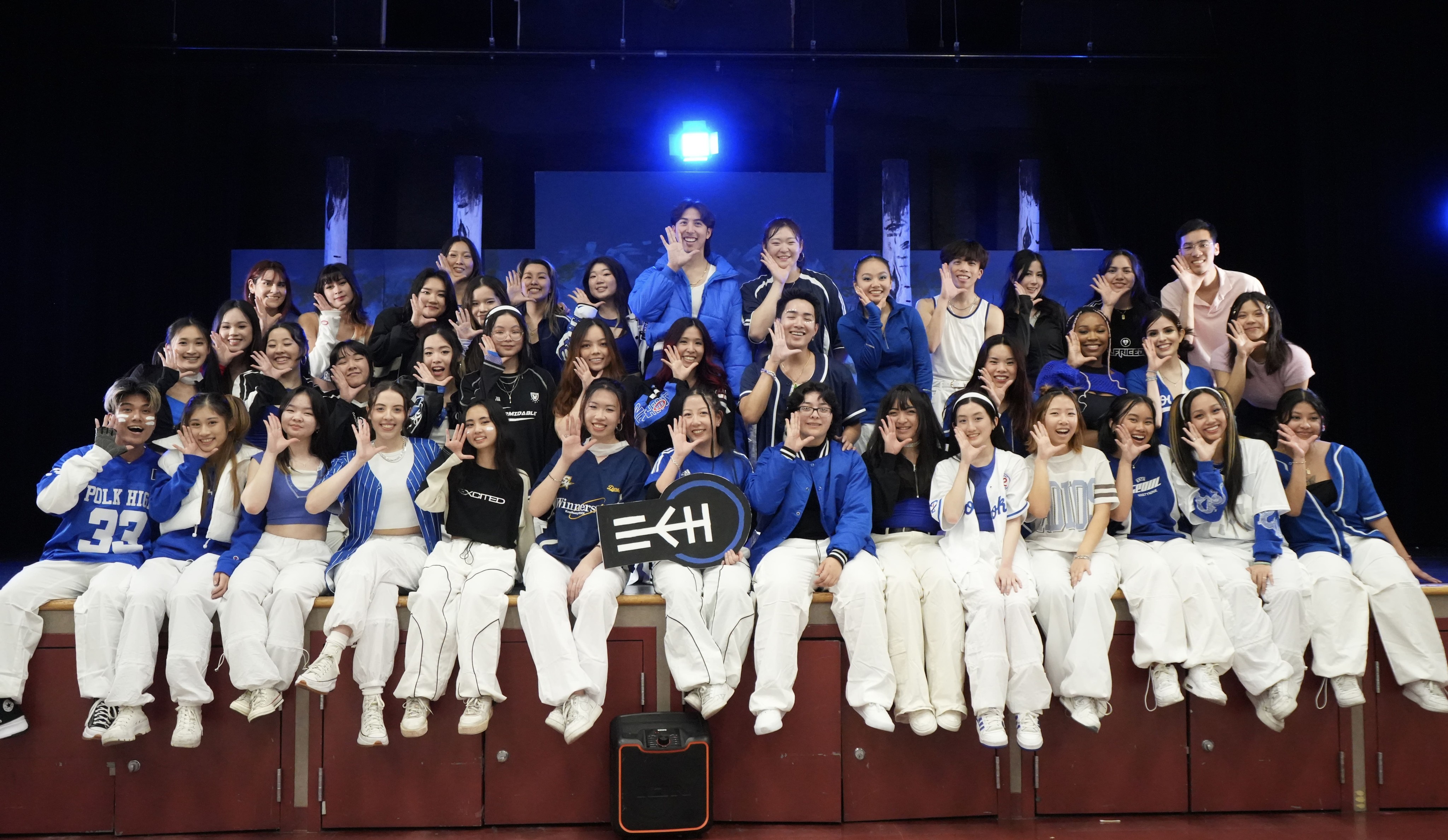 Large group of dance team members dressed in blue and white,posing for a group photo on a stage