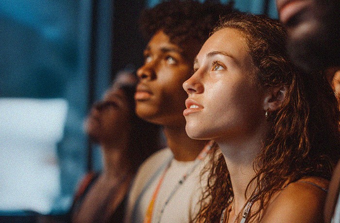 Students looking up attentively at a screen or presentation during a tech-focused activity or field trip.