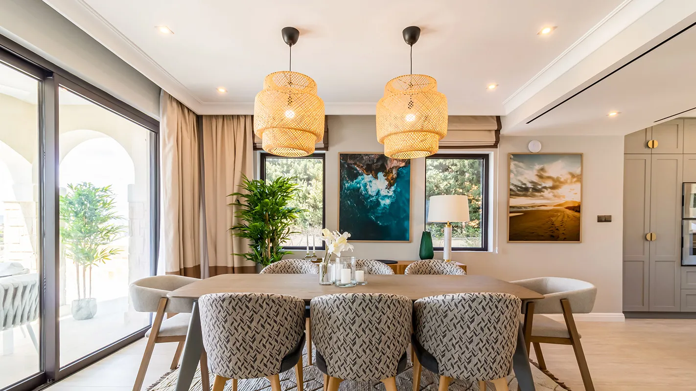 White Cedar House Mediterranean dining room with long table, woven pendant lights, and coastal artwork