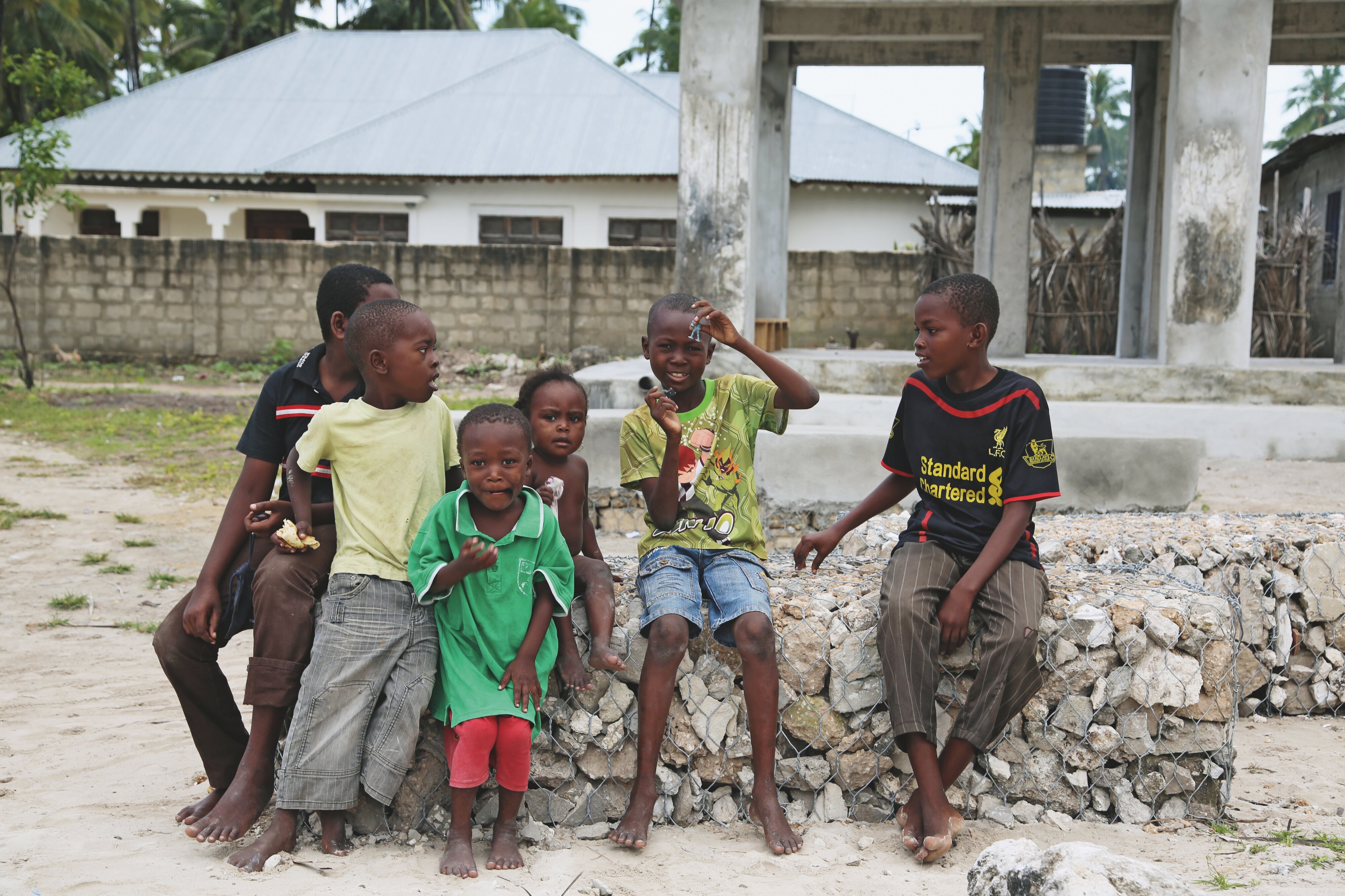 Gruppe von Kindern sitzt und steht lächelnd auf einer Steingabionenmauer vor Wohnhäusern