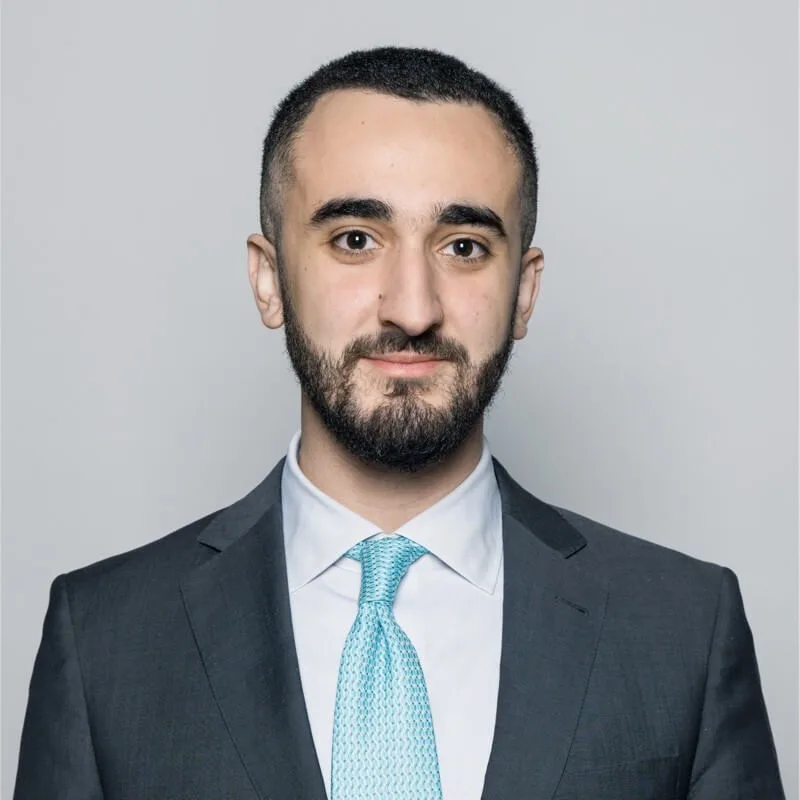A professional portrait of a man in a gray blazer and white shirt
