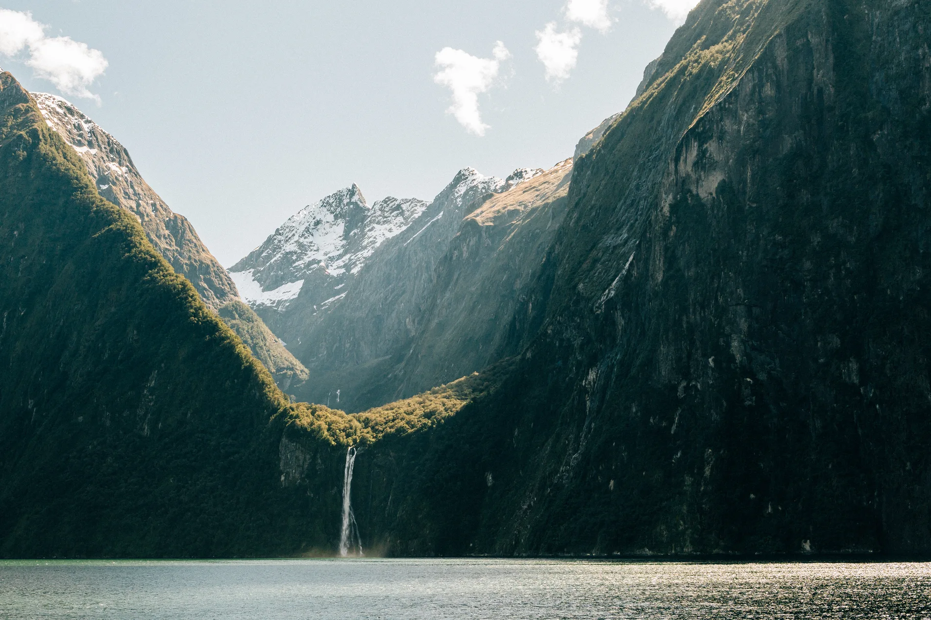 A waterfall dropping from a hanging valley into a fiord below sunlit peaks