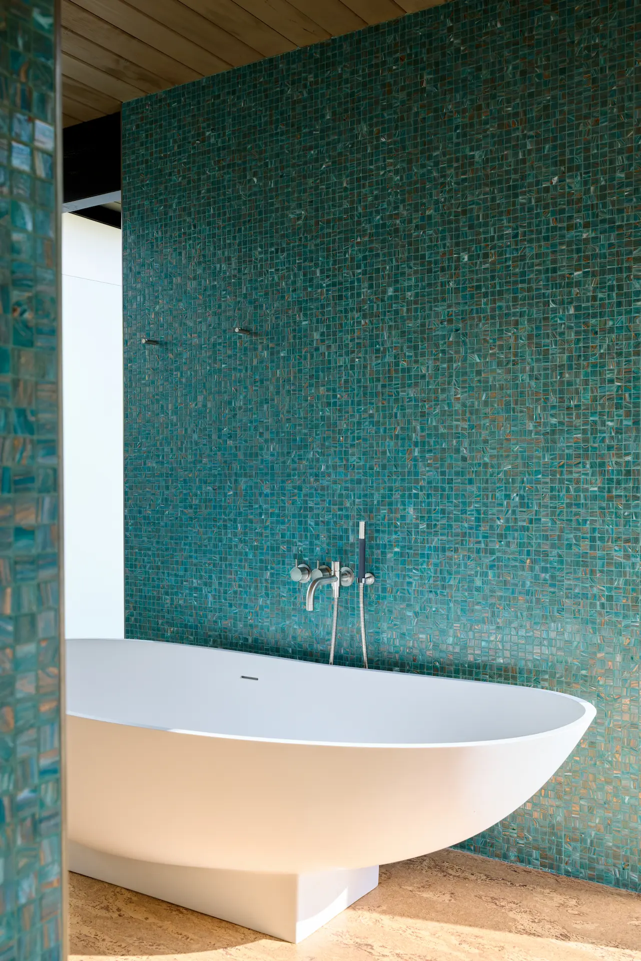 Portrait view of the master bathroom's free-standing tub from behind a corner, emphasizing the sleek design and luxurious feel in this Eichler remodel. Photo by Todd Huge.
