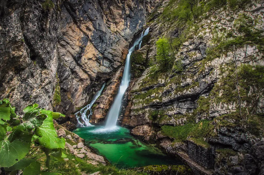 The unique double-stream Savica Waterfall cascading down a steep rocky gorge into a clear turquoise pool in the Triglav National Park.