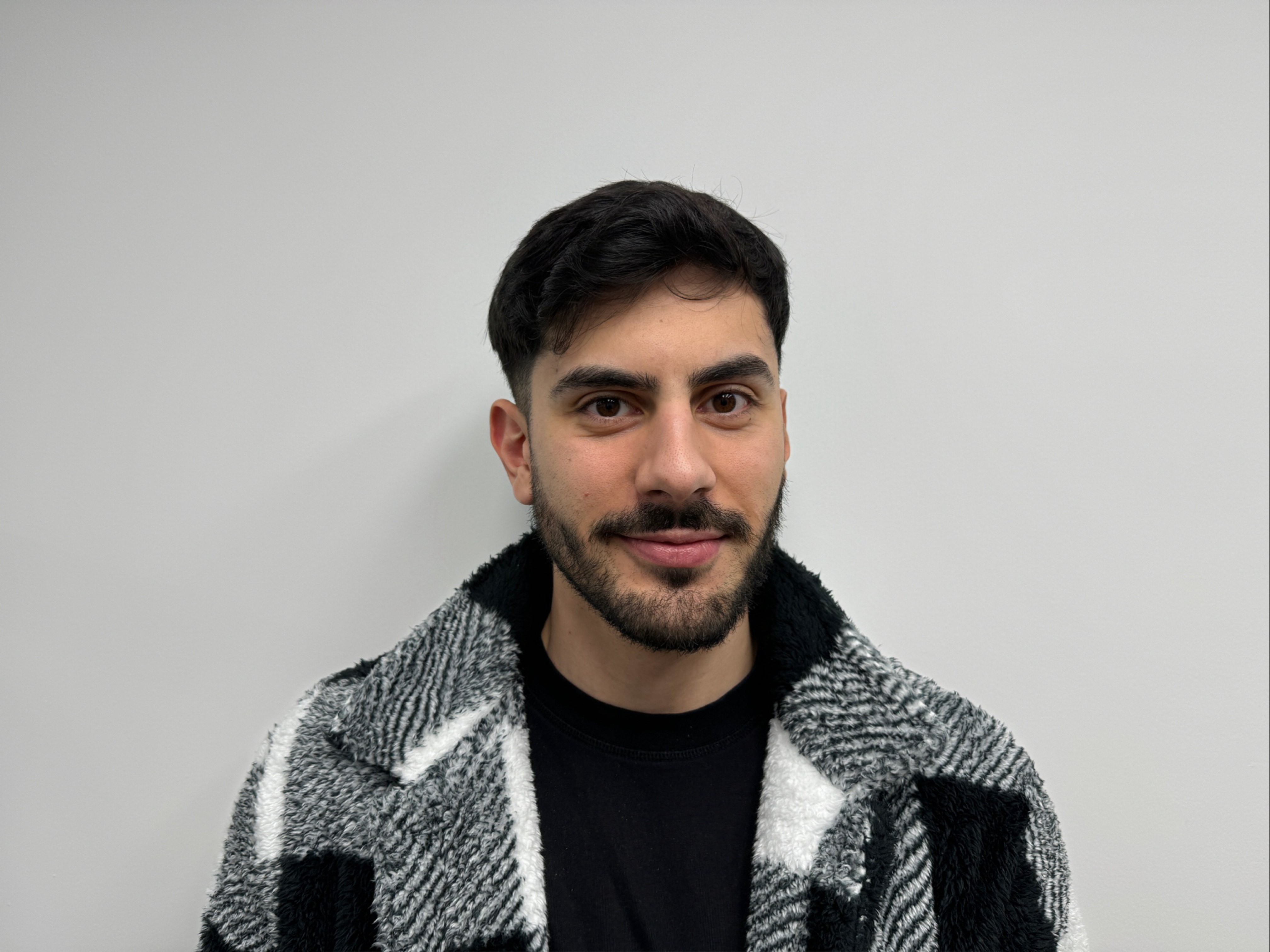 Portrait of a male product designer looking at the camera while wearing a black and white textured jacket.