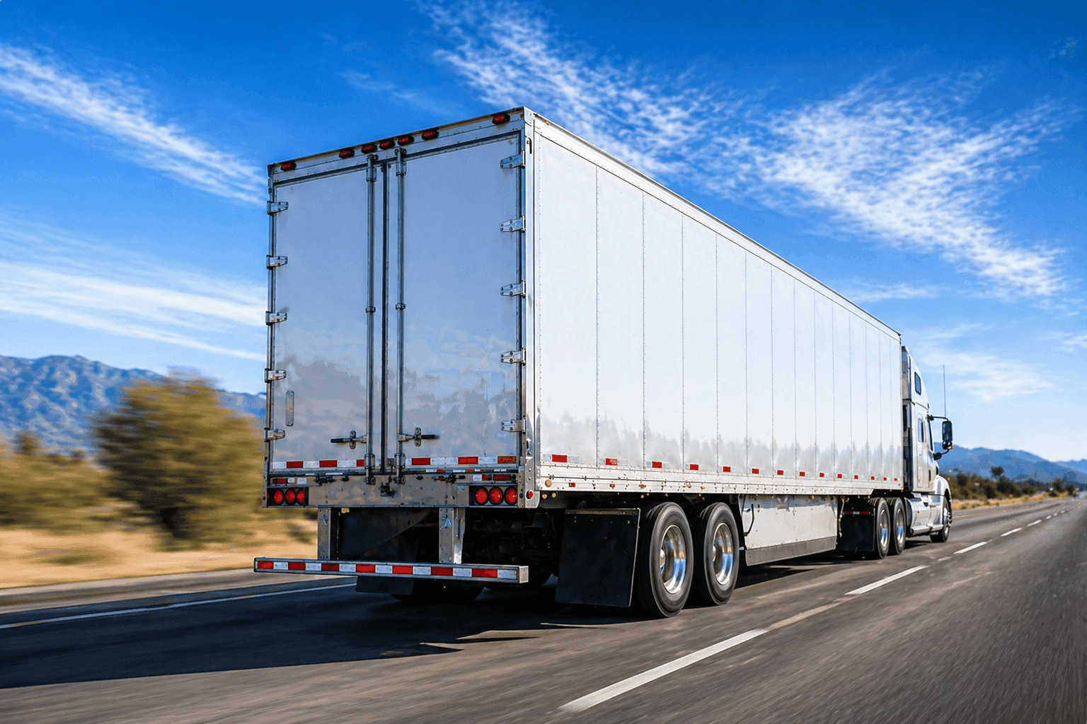 White semi truck driving on an open highway with mountains in the background, showing a full truckload shipment in transit.