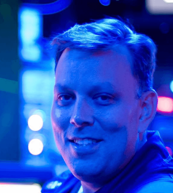 Smiling individual in a dimly lit environment with blue and red lighting, showcasing a friendly demeanor.