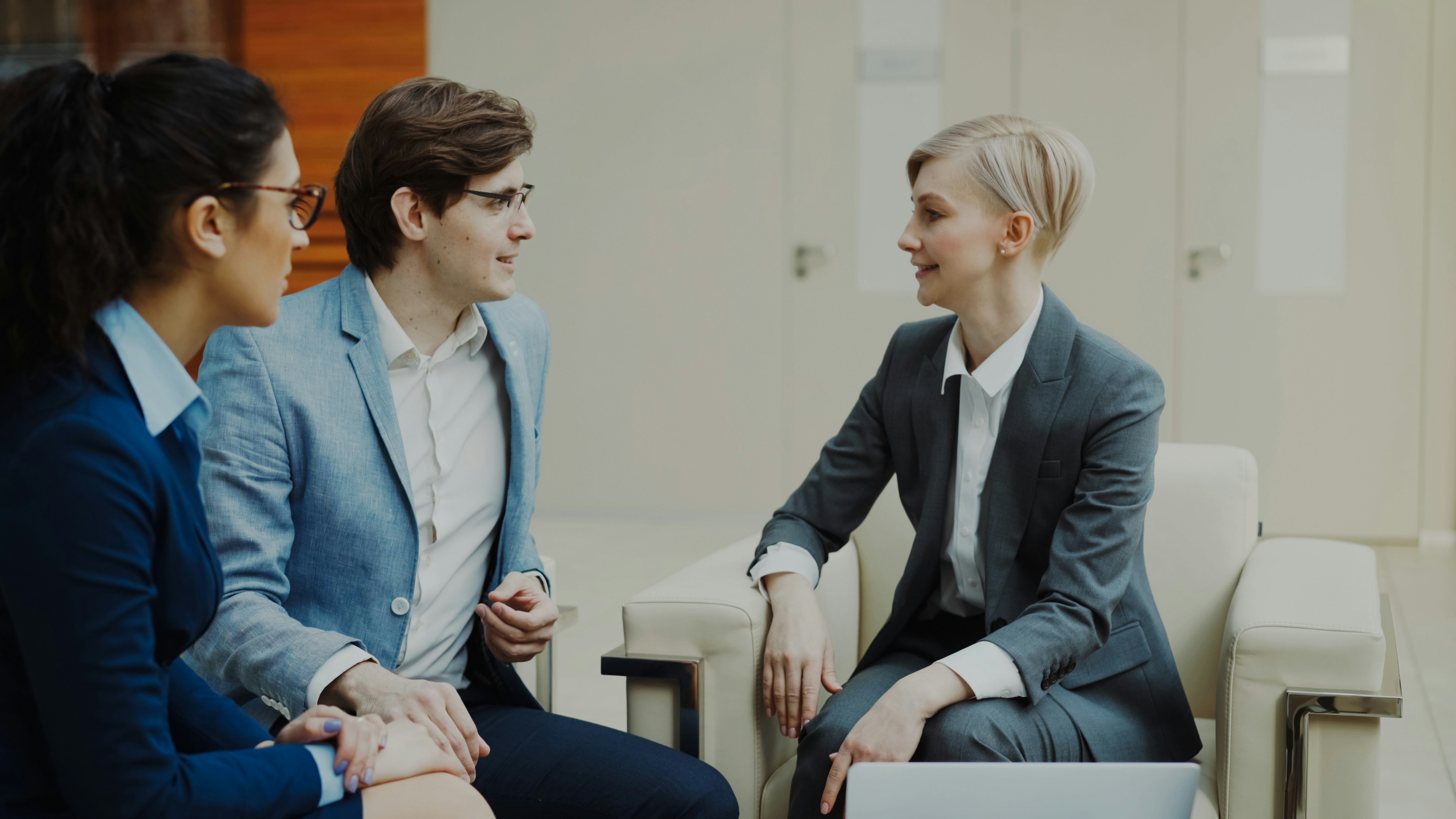 Three professionals in business attire conversing indoors.
