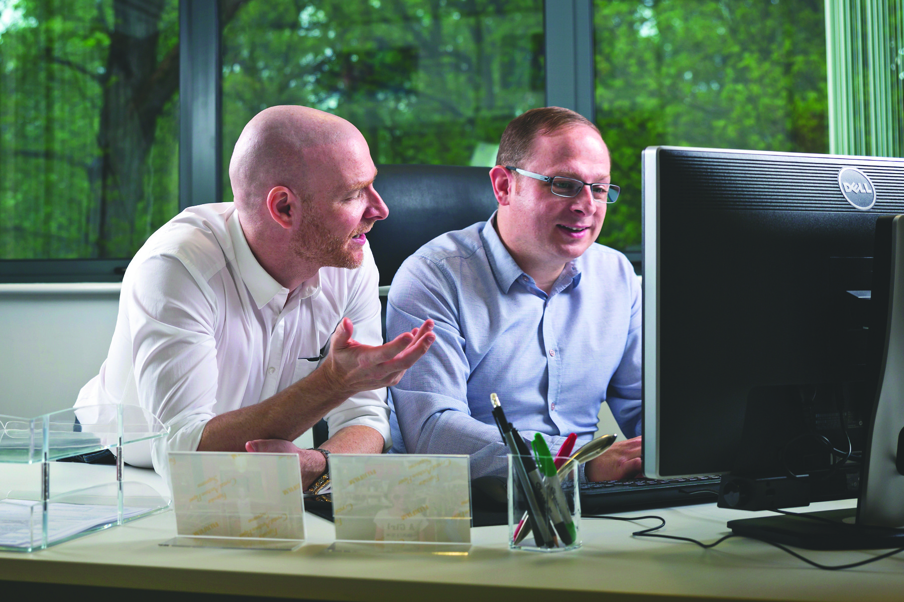 Two men working at a desktop computer together.