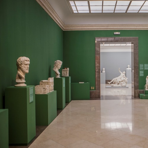 博物館的展廳有綠色牆壁、大理石地板,展示著放在綠色基座上的白色古典雕塑,以及下一個房間中的大型雕塑。