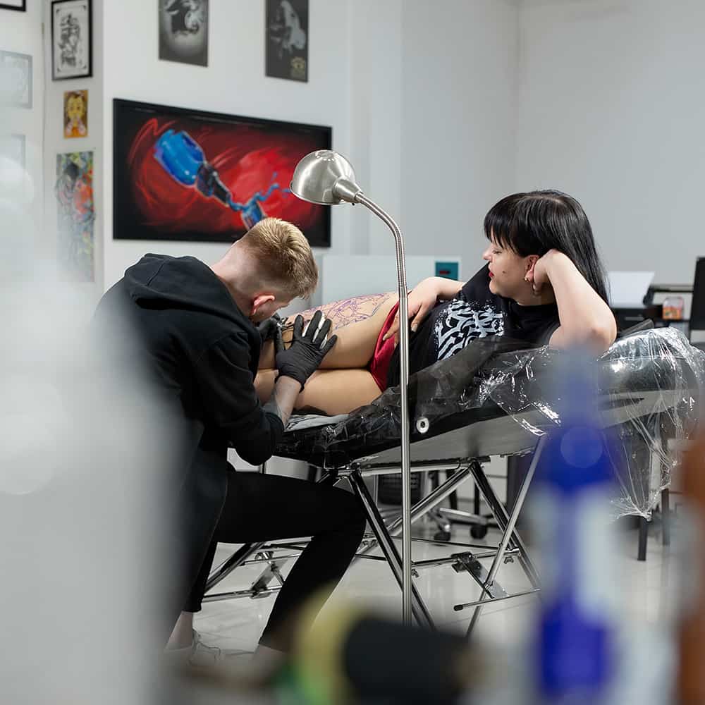 Close-up portrait of a person wearing a gray insulated hooded jacket with the hood up, showing their face framed by the hood against a light background.