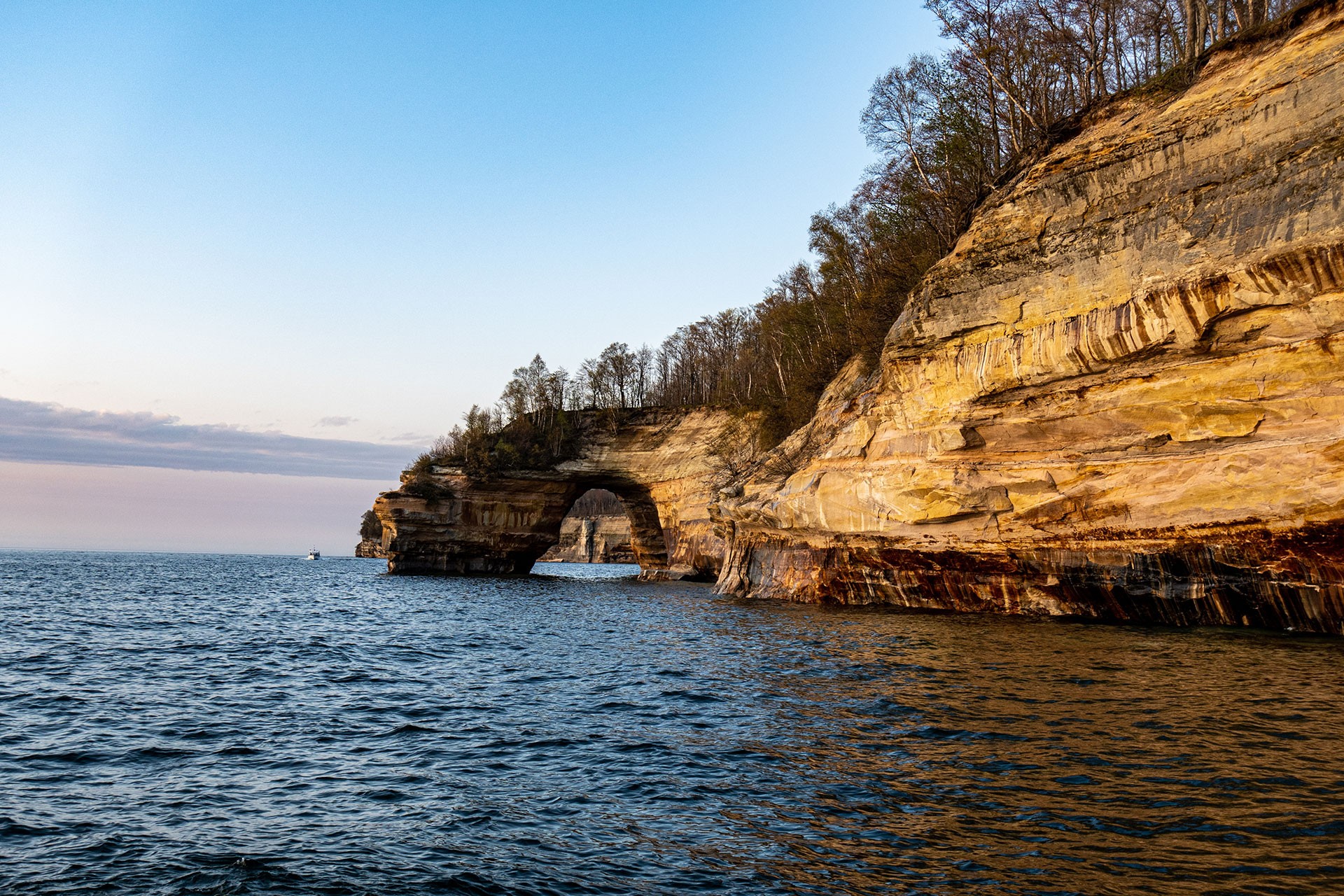 A natural rock arch potrudes into the water with a gradient sky in the background