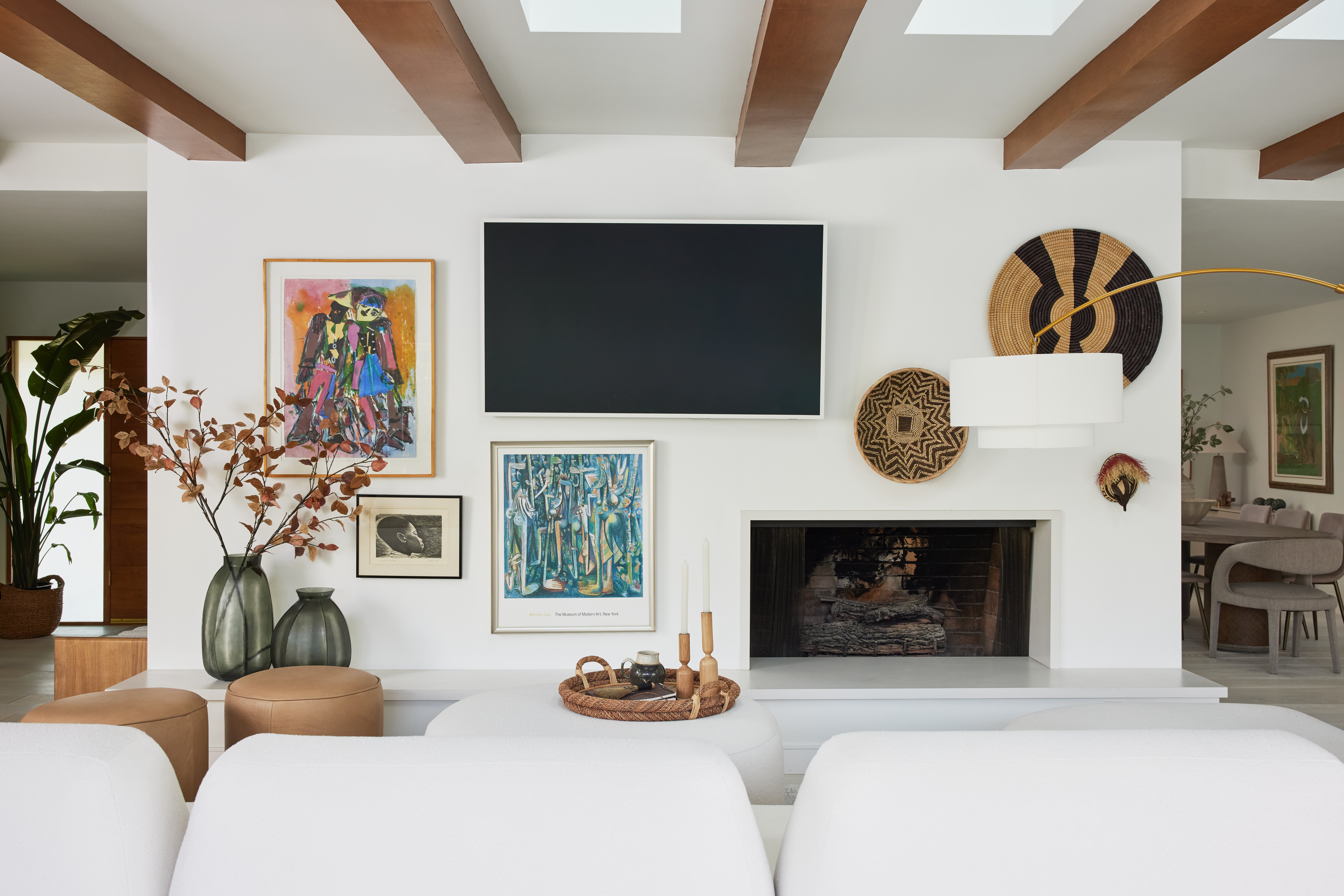 Airy family room with exposed beams, off-set fireplace, white boucle modular sofa, round tan ottomans, and heritage art pieces by Jubilee Interiors in Los Angeles, California 