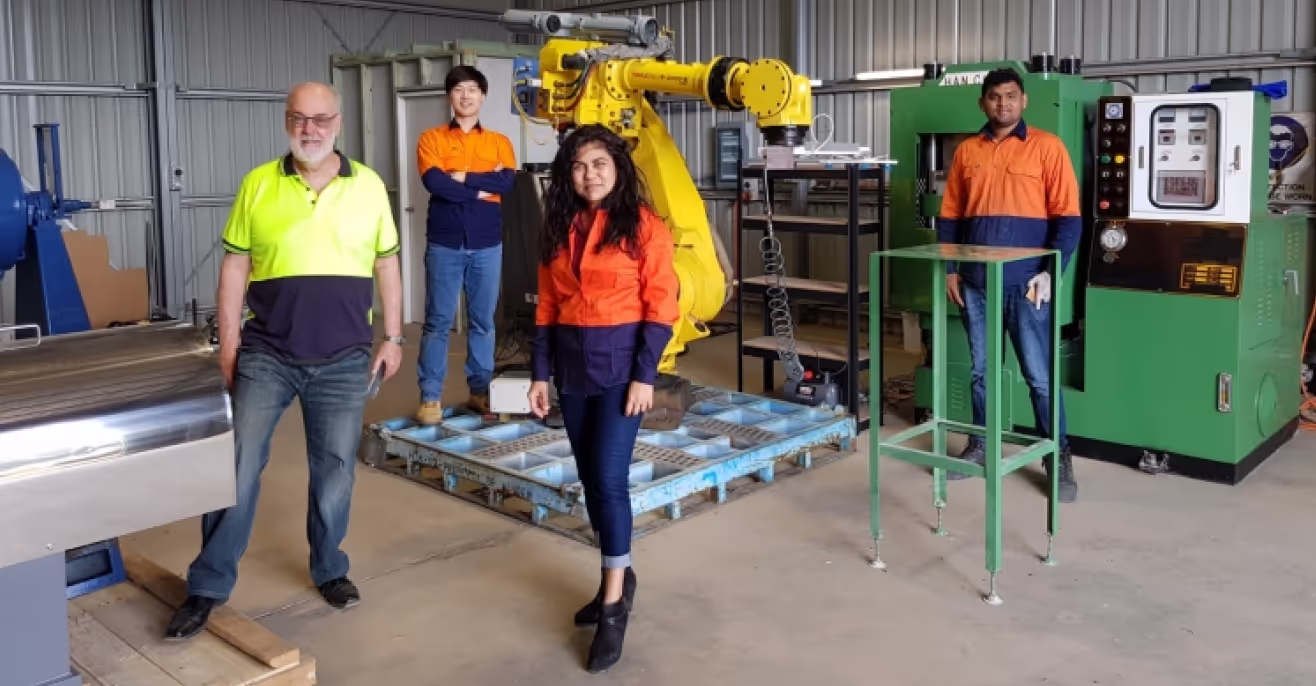Veena Sahajwalla with SMaRT Centre colleagues in high-visibility workwear inside a MICROfactorie, beside a robotic arm and tile moulding trays