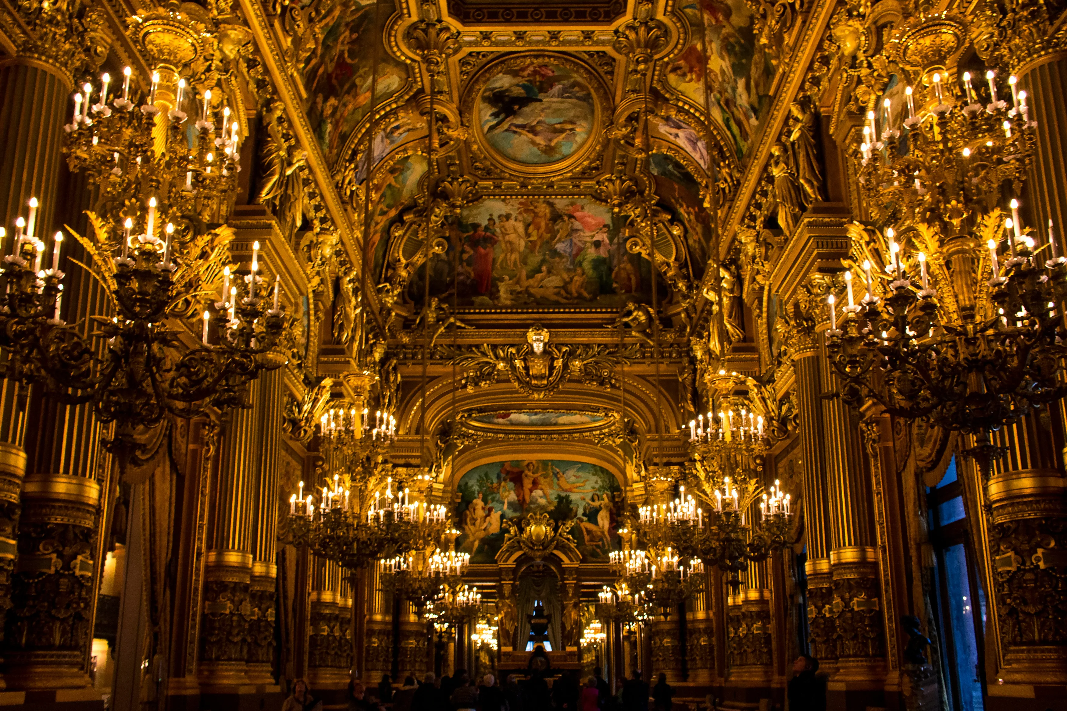 Looking down the extremely ornate and chandalier filled hall of the Palais Garnier in Paris, with art prominently featured on the ceiling.