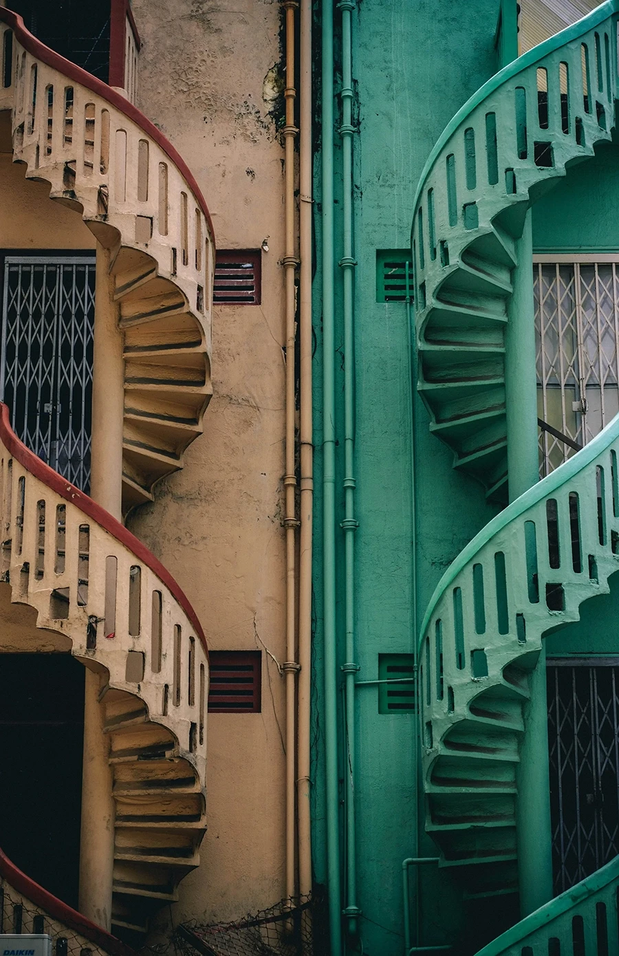 Two adjacent spiral staircases on contrasting beige and green building walls.