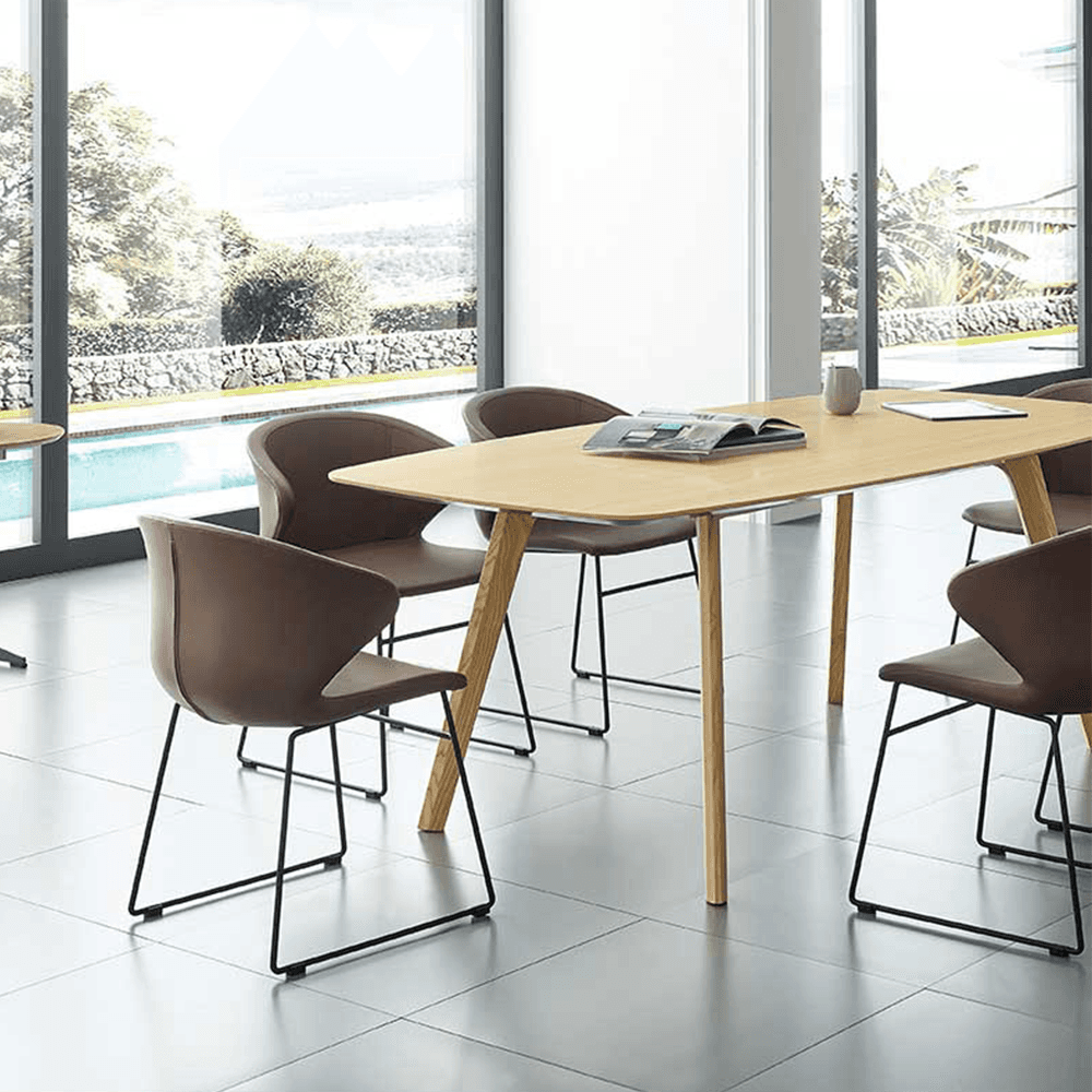 Set of dark brown leather executive chairs with black sled bases positioned around a natural wood boardroom table in a sunlit room with floor-to-ceiling windows and a pool view.