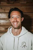 Glimlachende man met donker haar in een lichte Broederschap-hoodie voor een houten wand