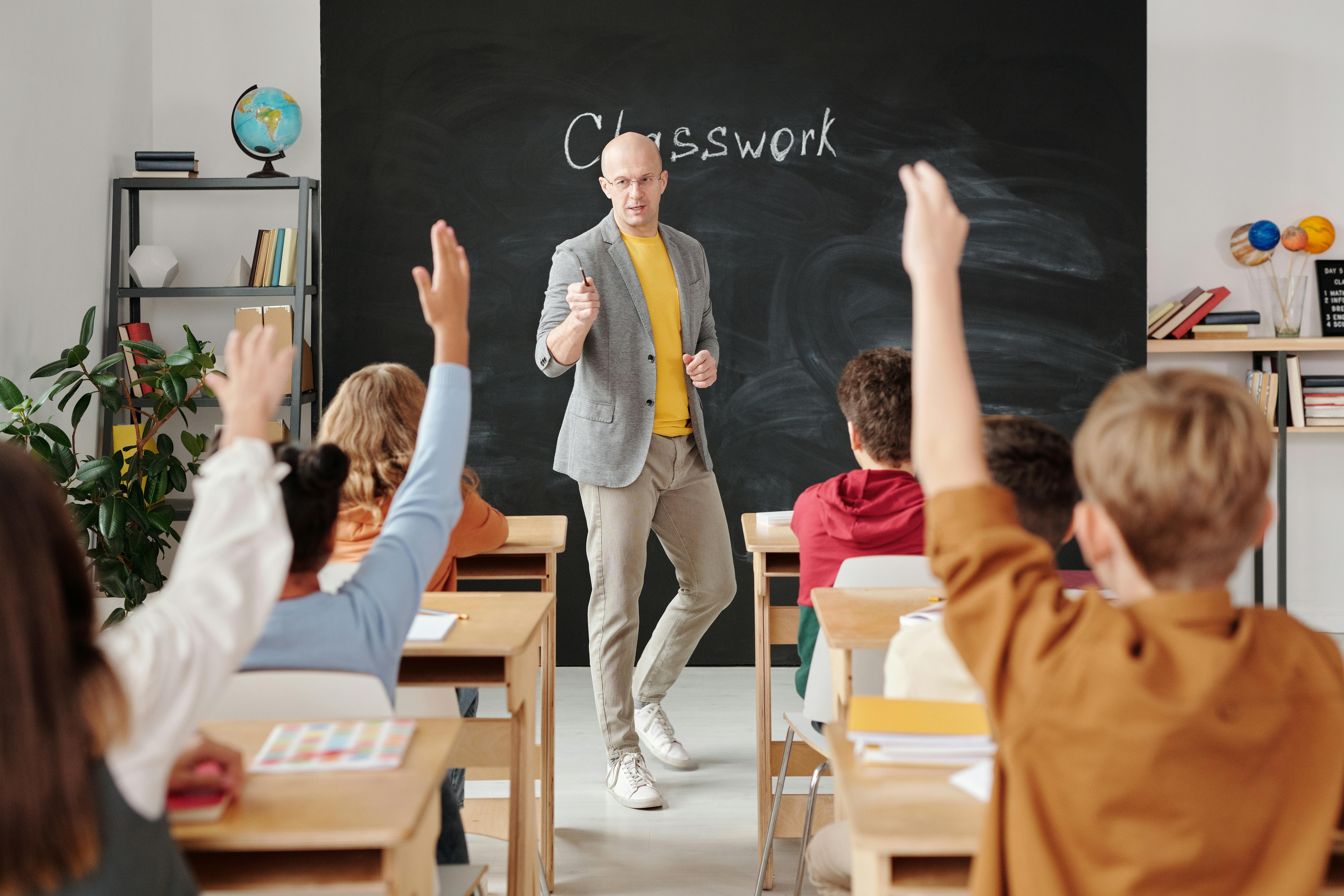 Teacher Teaching His Students, this image features students raising their hands