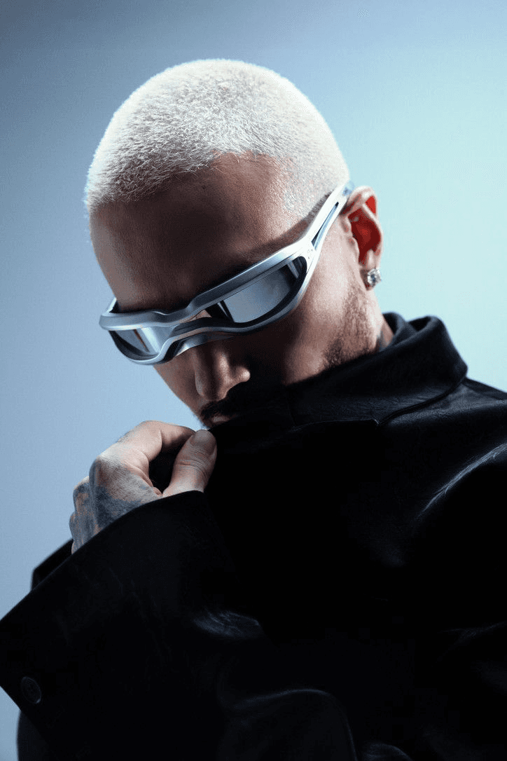 Studio portrait of a man with a bleached buzz cut wearing futuristic silver sunglasses and a black leather jacket