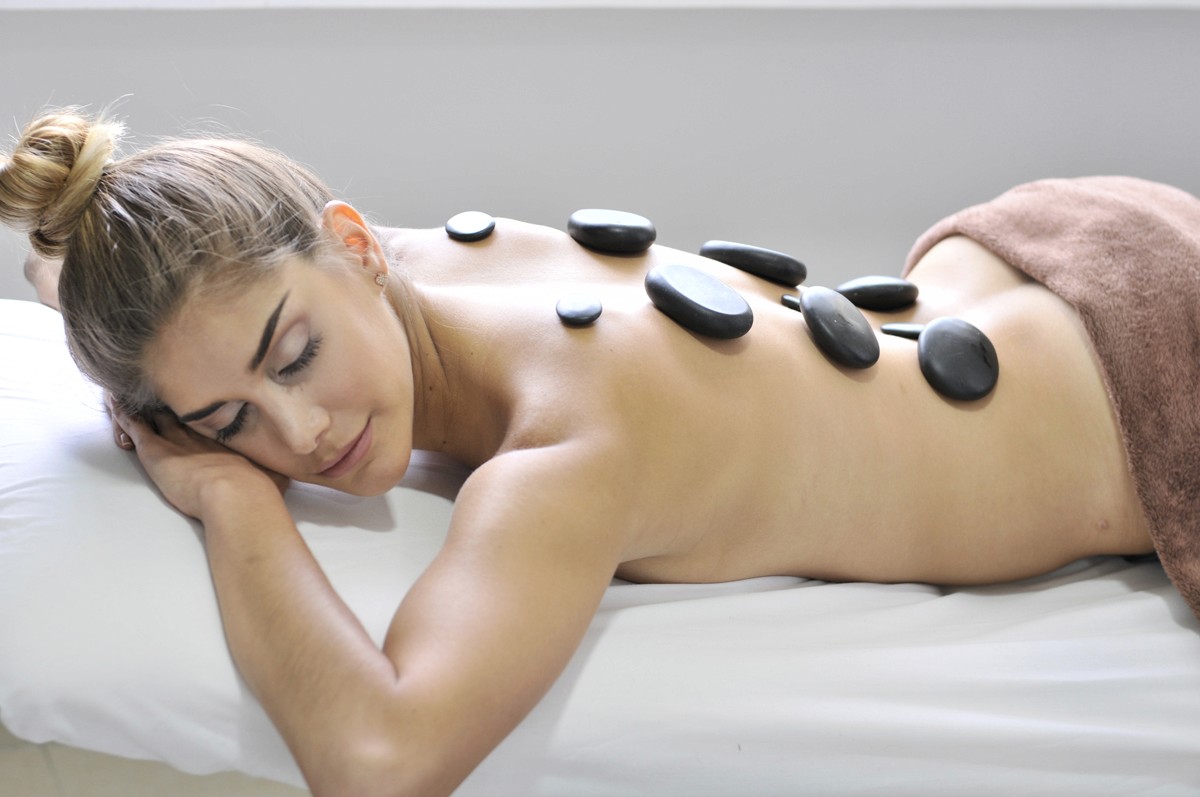 A woman lying down with a towel wrapped around her head, her face glowing with facial oil. She has a peaceful expression, enjoying a skincare treatment.