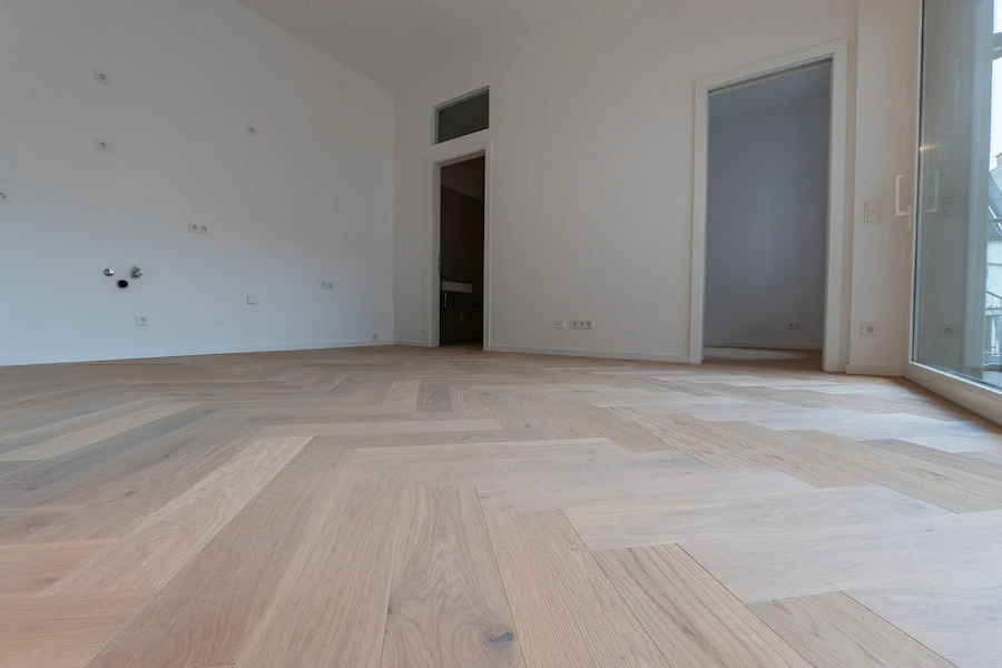 Unfertiger Innenraum mit frisch verlegtem, unbehandeltem Fischgrät-Parkettboden vor der endgültigen Oberflächenbehandlung.