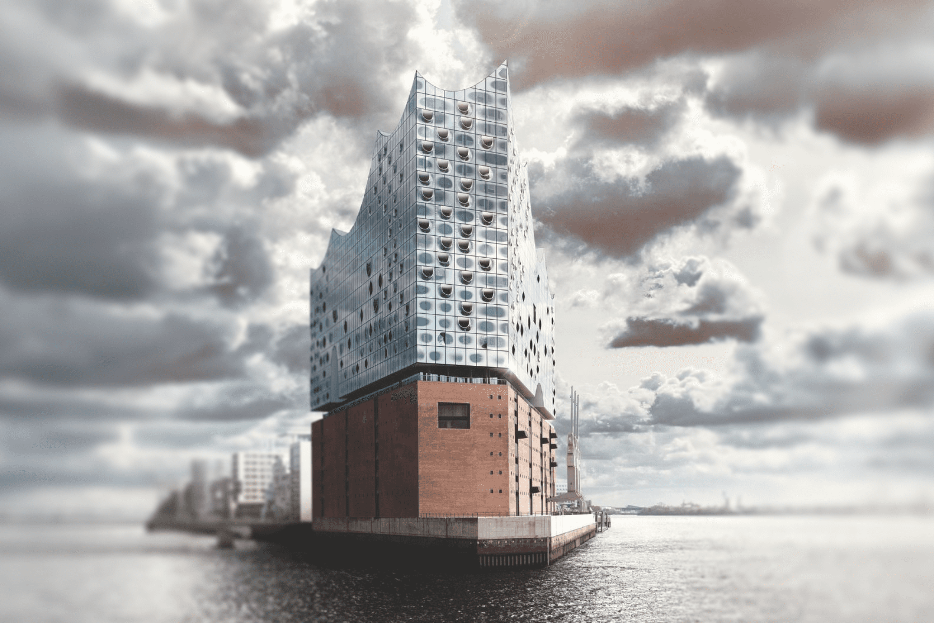 Modern concert hall with glass facade and brick base on waterfront.
